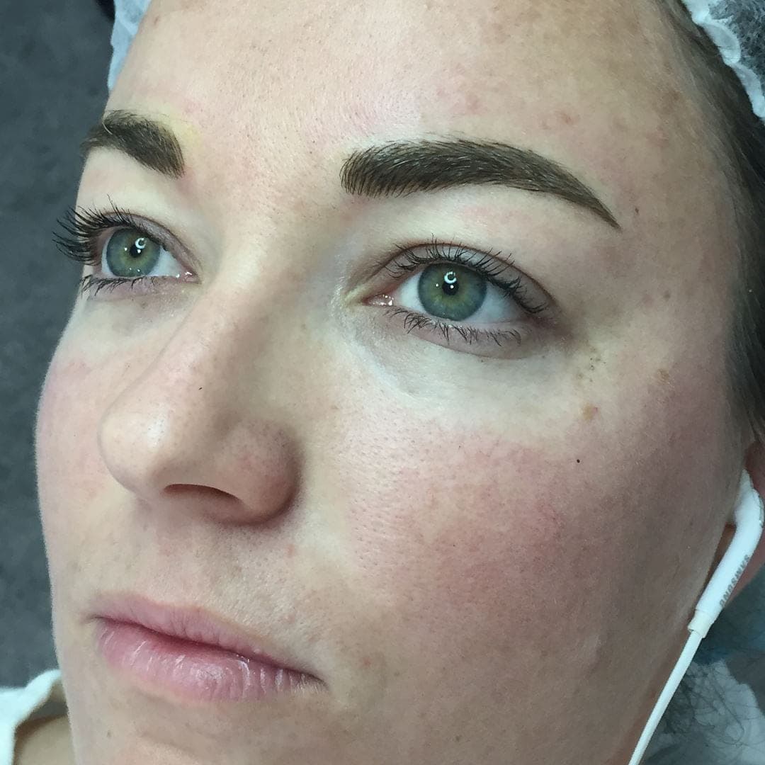 Freshly tattooed hair-stroke brows on a client with green eyes