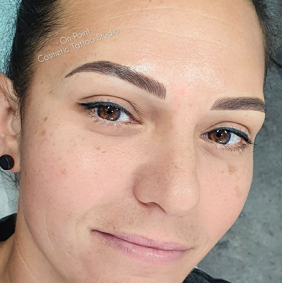 A client with tattooed eyeliner and brows, looking at the camera