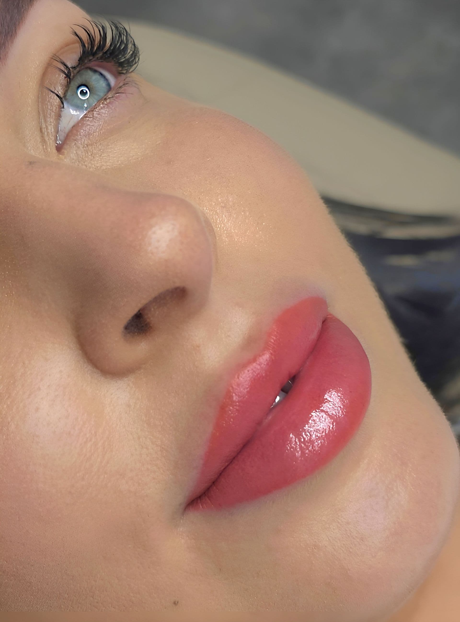 Freshly tattooed lips in a soft rose, seen from below